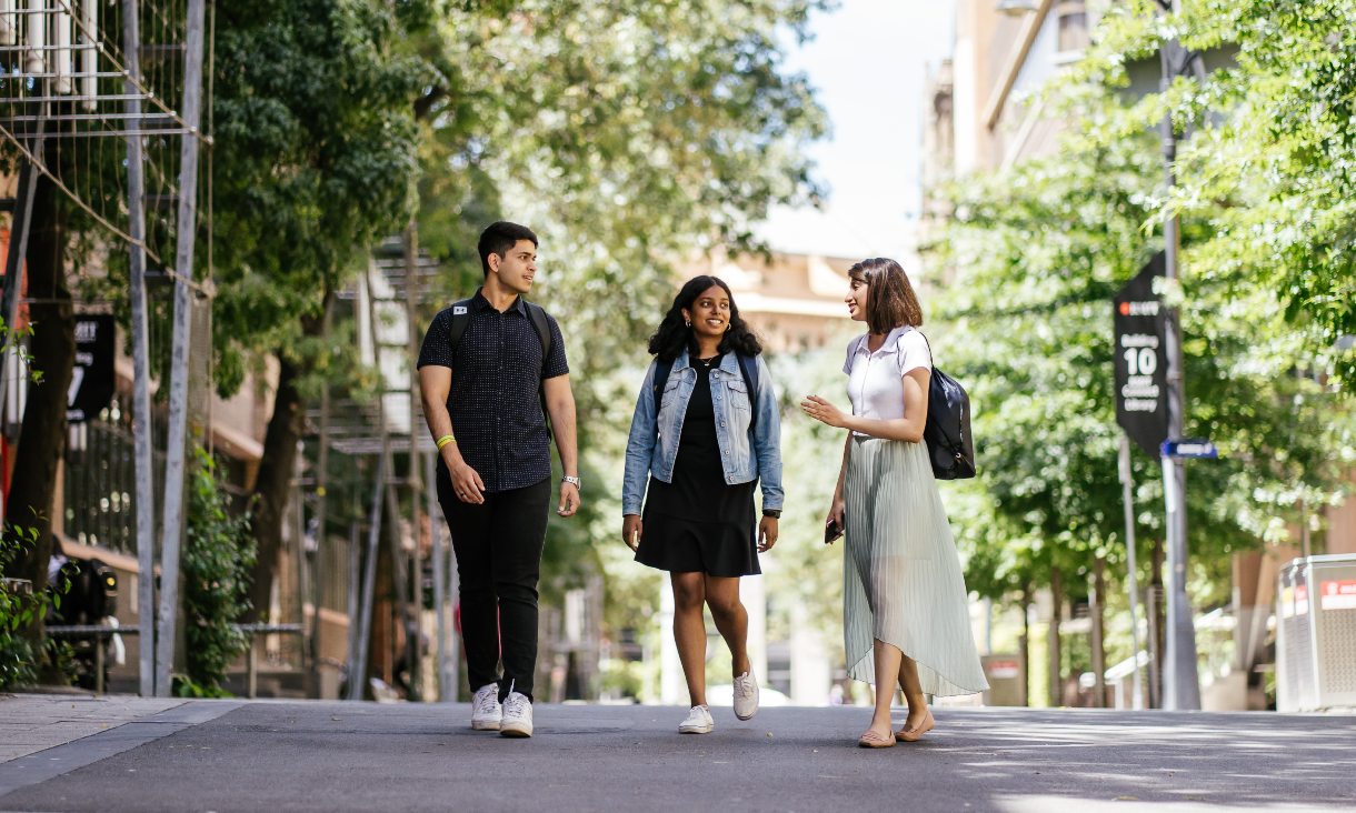 Three students walking down a street having a conversation.
