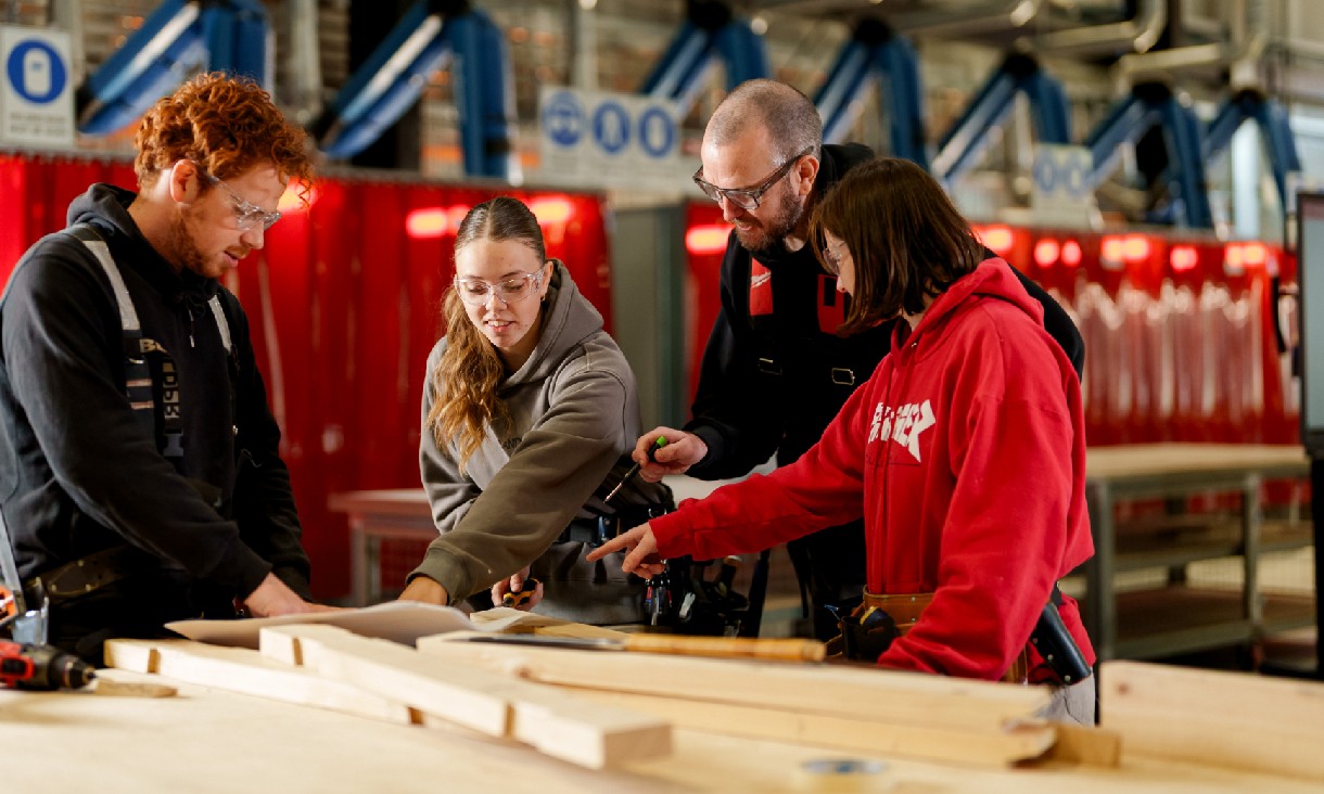A teacher assists 3 students with carpentry.