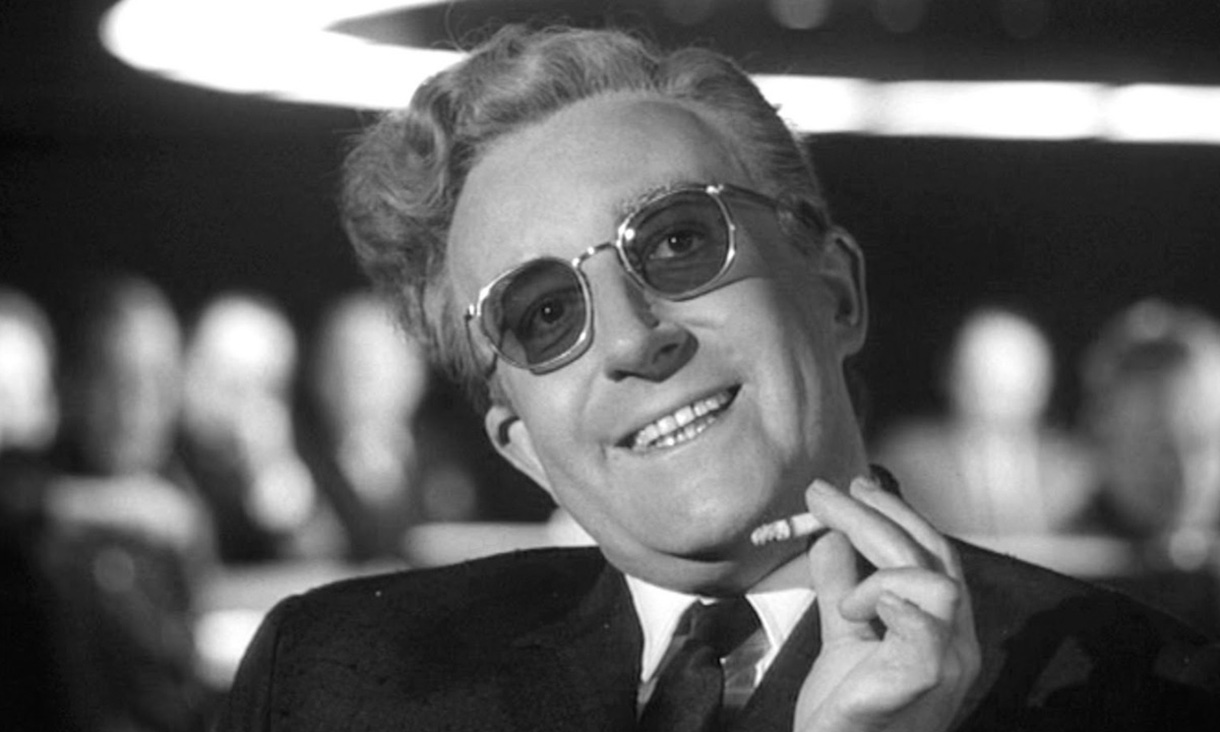 Person in a suit sitting at a table in a black and white setting, with blurred people in the background suggesting a formal or professional environment.