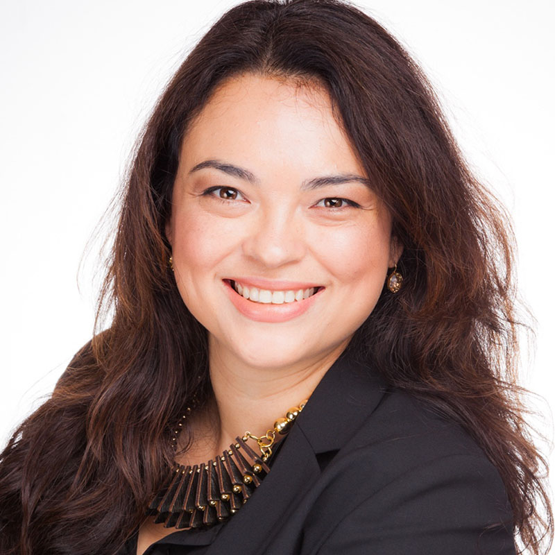 Photograph of Lydia. She smiles directly at the camera. She has long, dark brown hair and wears a black shirt.