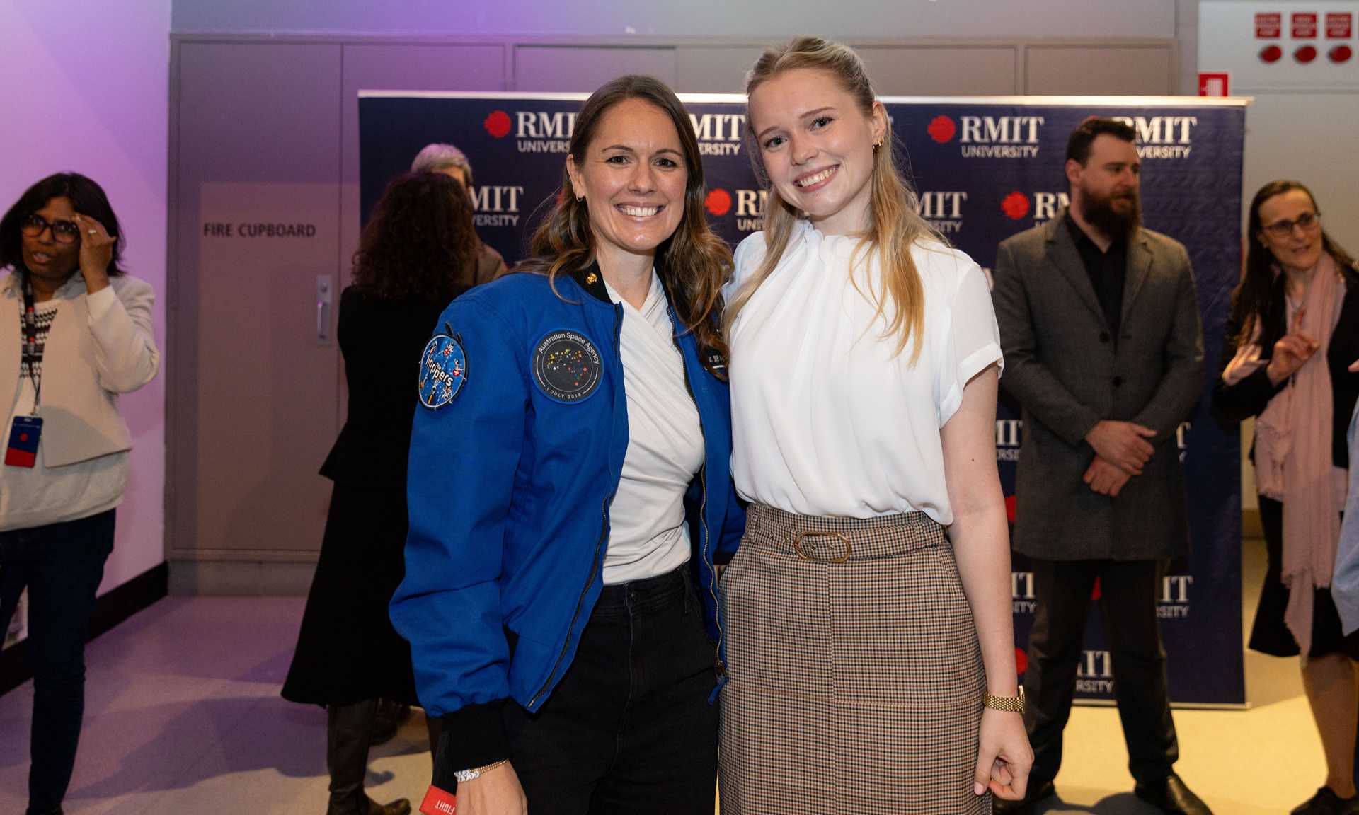 Two attendees smile together at an RMIT University event, highlighting achievement, collaboration and inspiration. One wears a mission-style jacket, reflecting innovation, leadership and the university’s strong connection to space and aerospace.