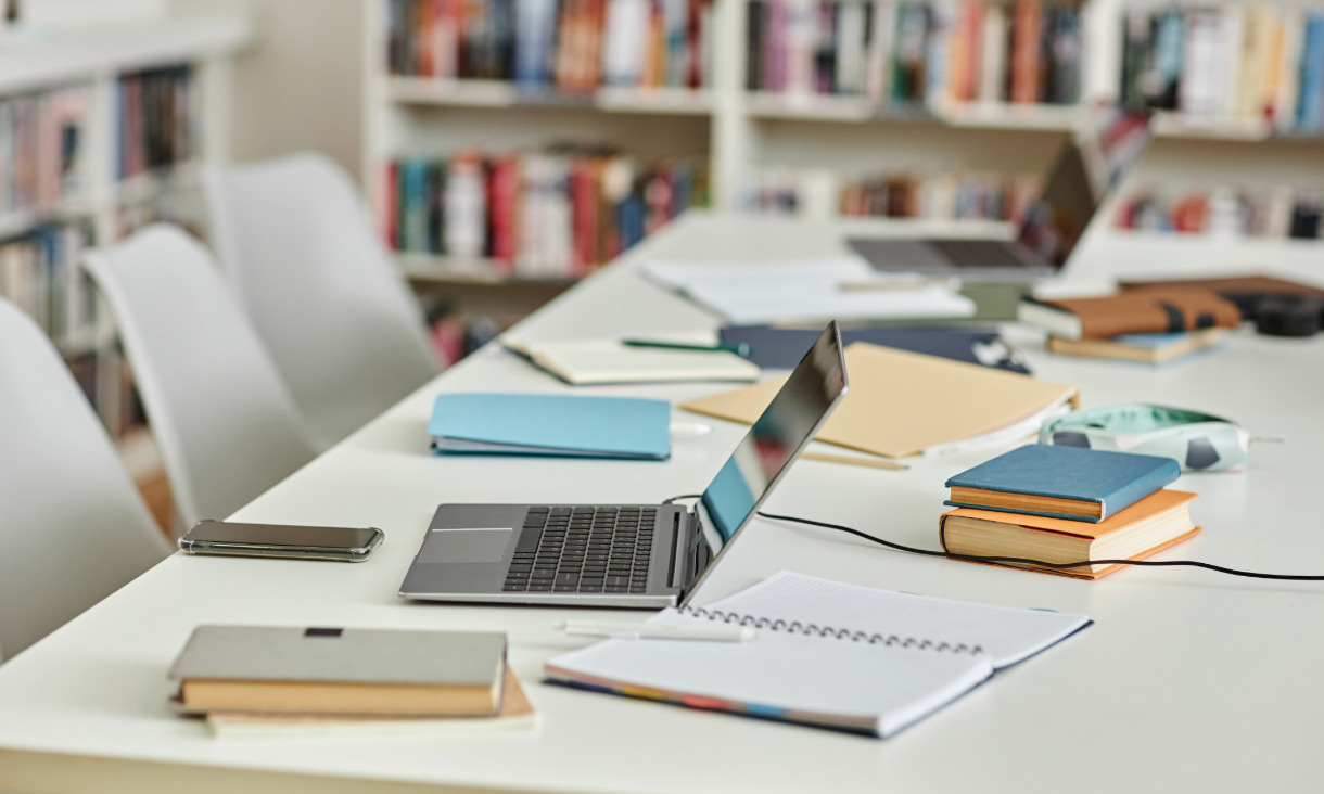 Banner image of a desk in a library with laptops and books