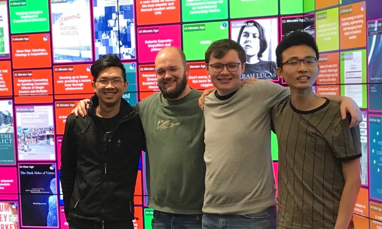 Four male student standing in front of the Library Live screen.