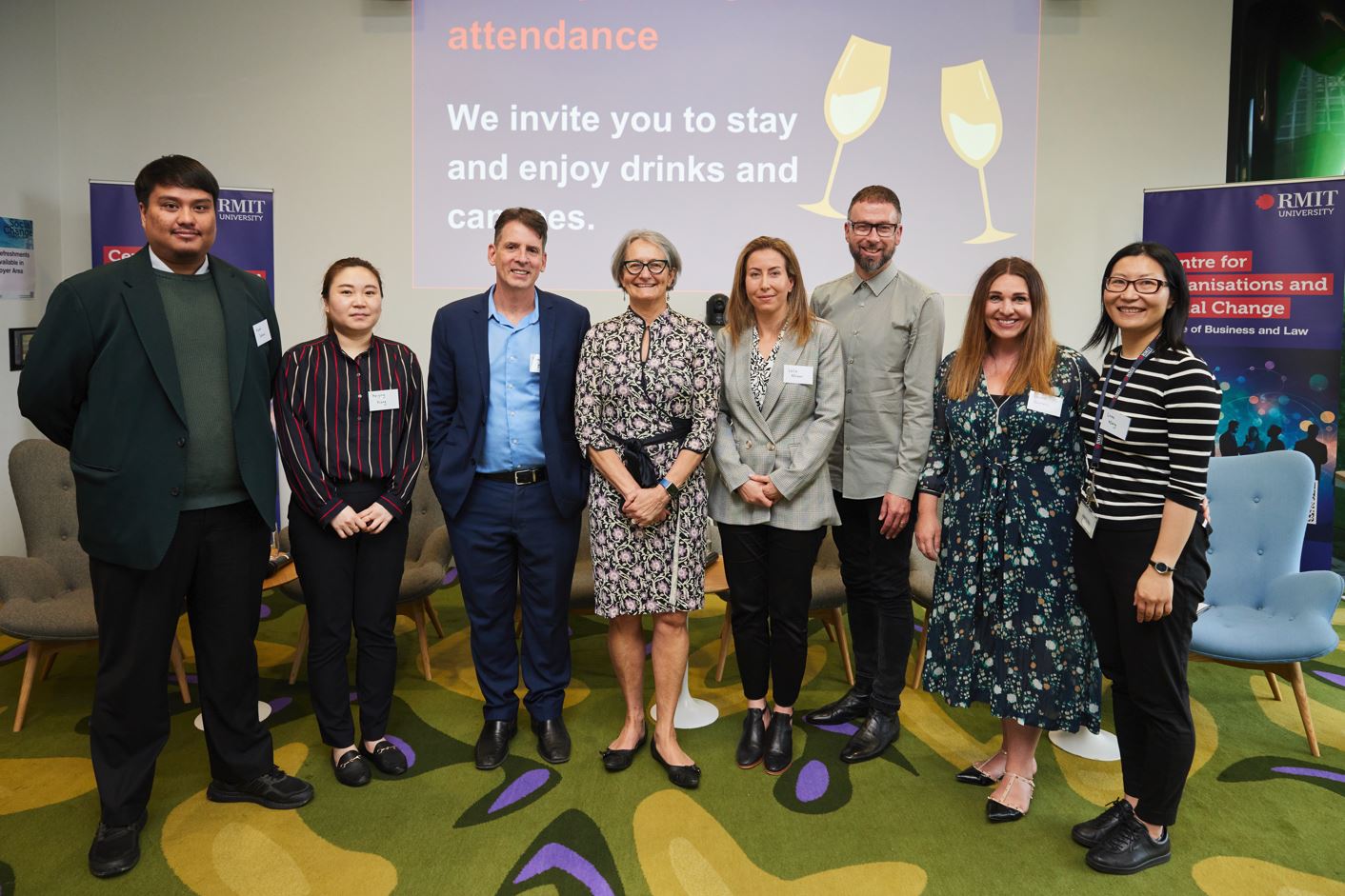Group of men and women stands in a row facing the camera and smiling