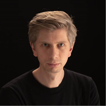 A man in front of a black background is looking directly at the camera 