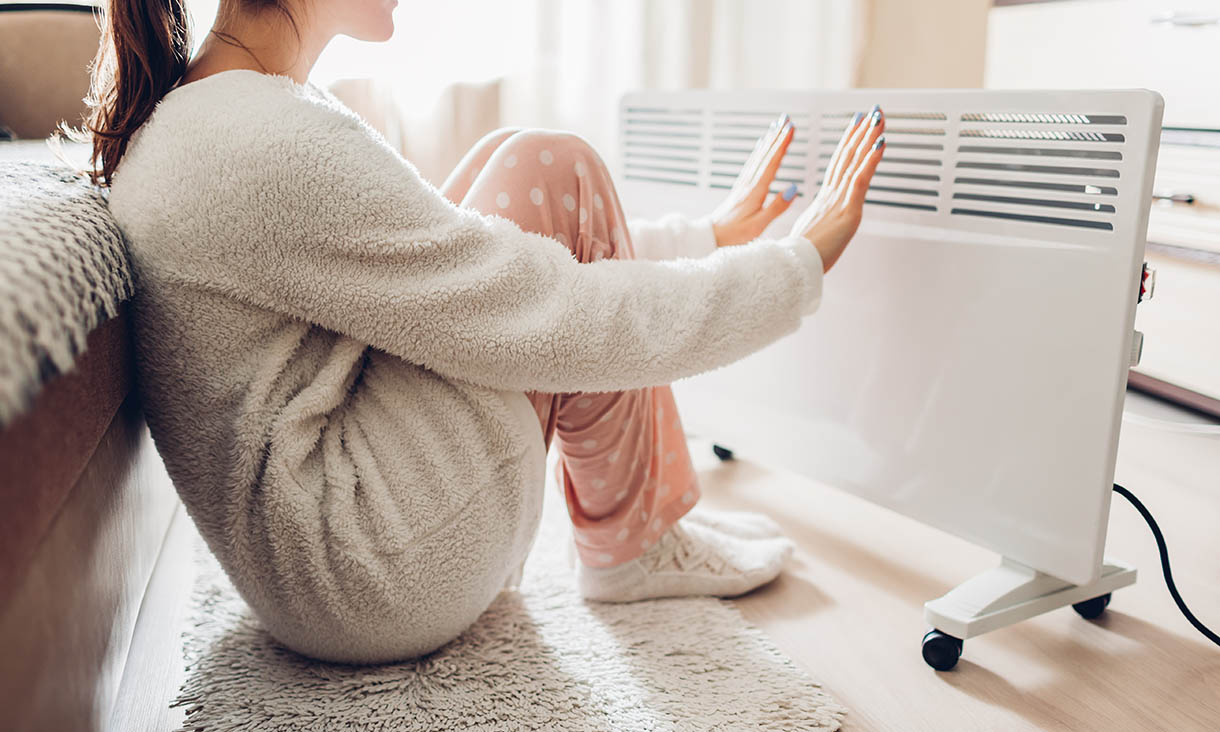 Woman warming her hands sitting by device and wearing warm clothes
