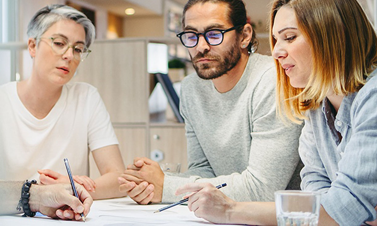 4 people in a meeting room making plans on a piece of paper. 