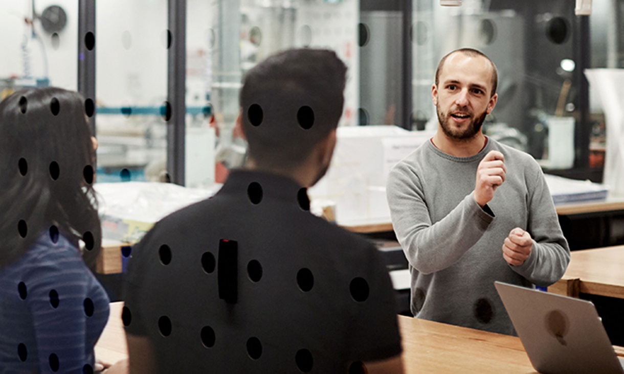 A man explains something during a meeting with two other people.