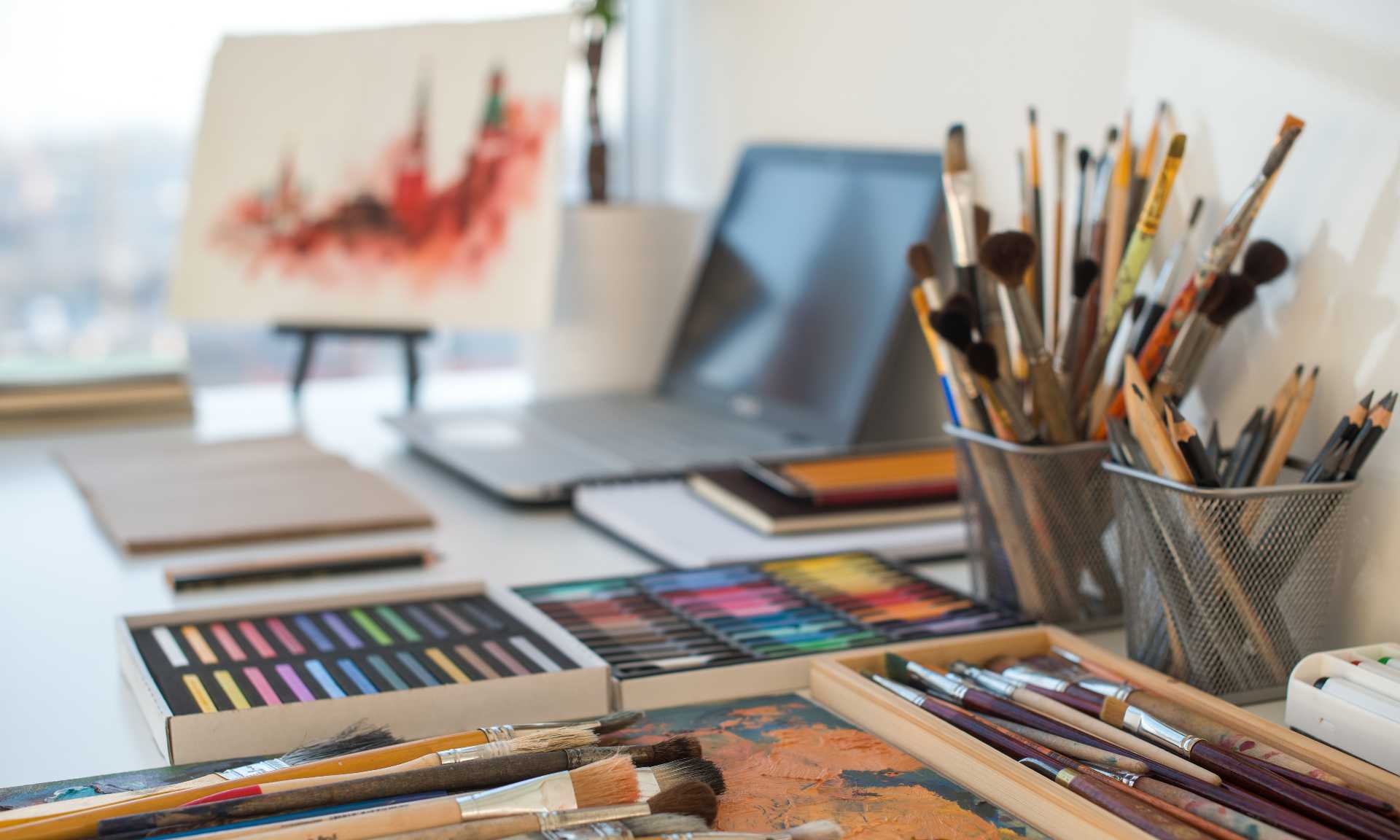 Art supplies and brushes and laptop on desk