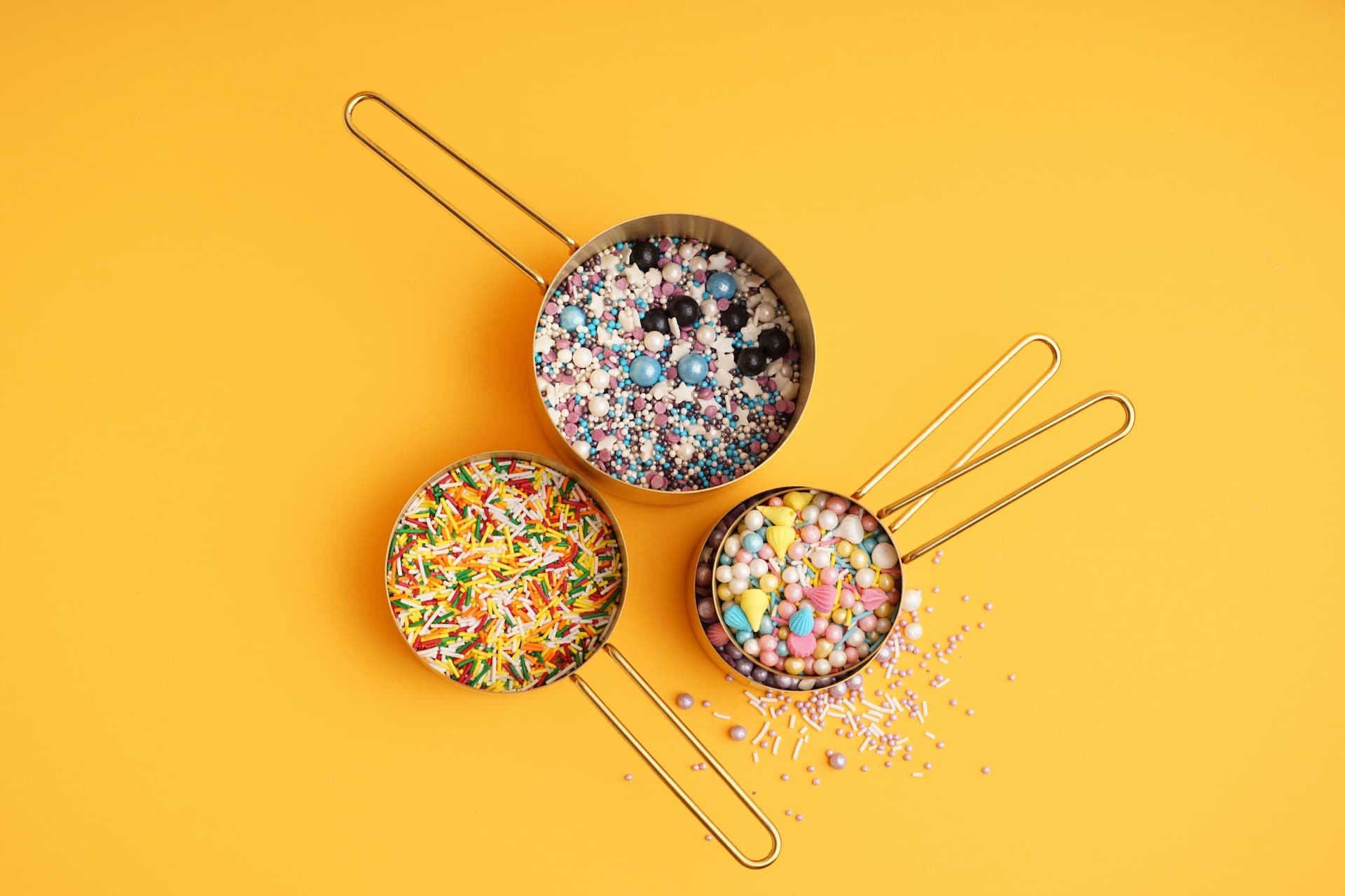 Measuring cups with sweet colorful sprinkles on orange background