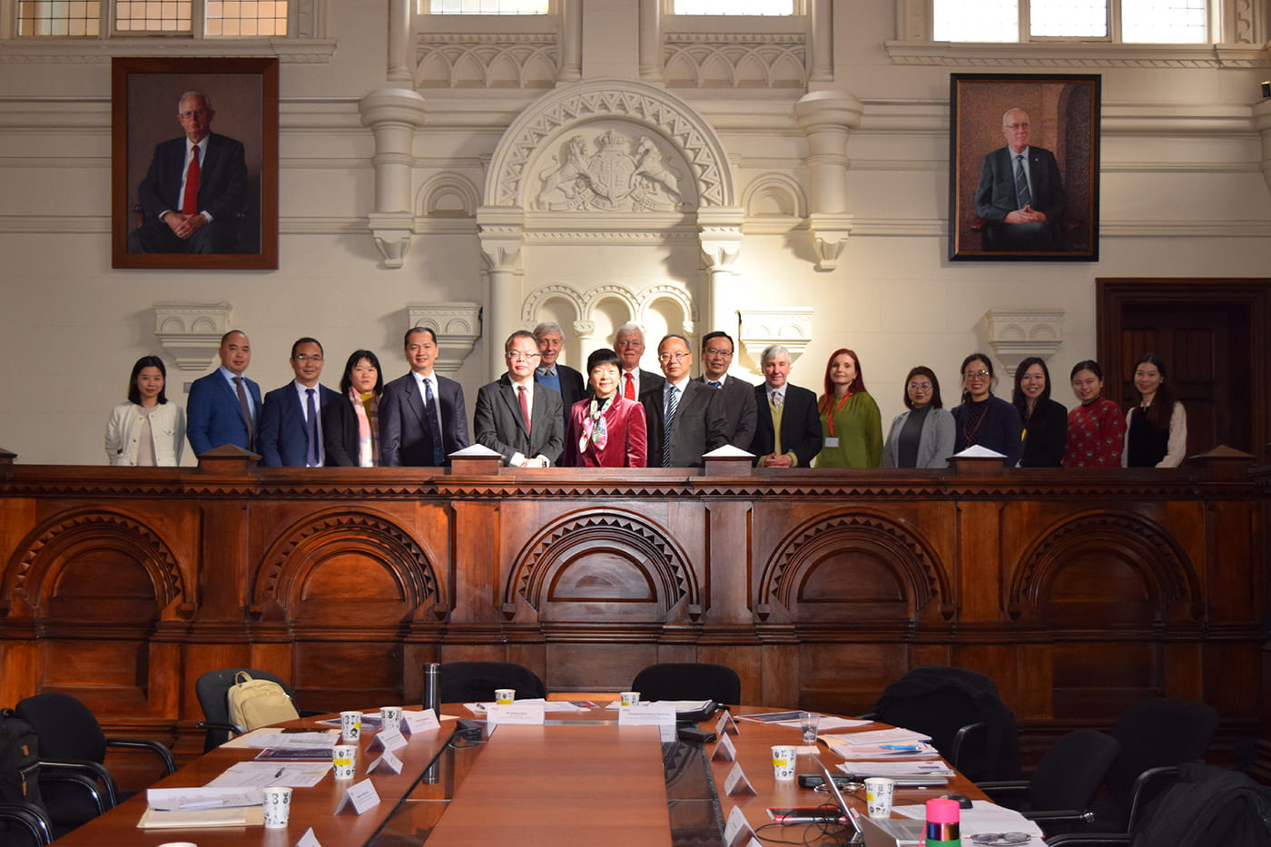 A group of people standing in a line in an old courtroom with large portraits of old white men on the rear wall.