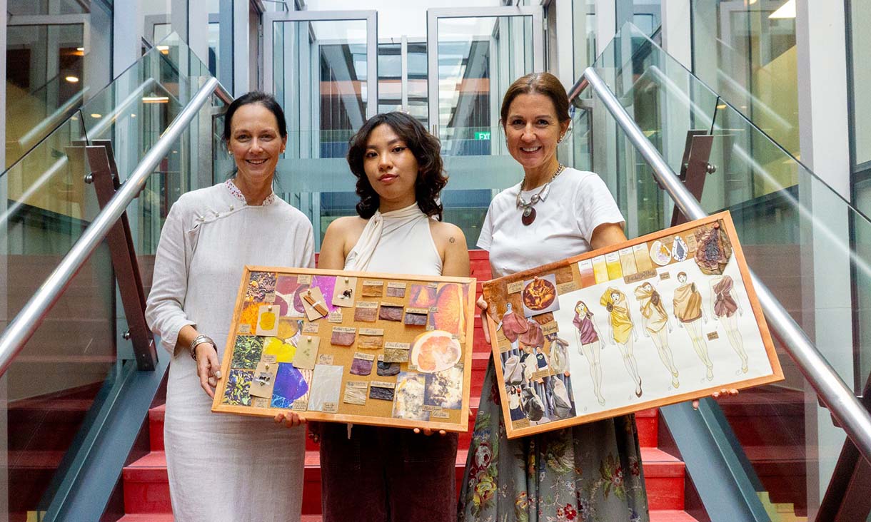 Photograph of Veronica, Corinna and Donna standing together. They're holding boards that display colourful illustrations.