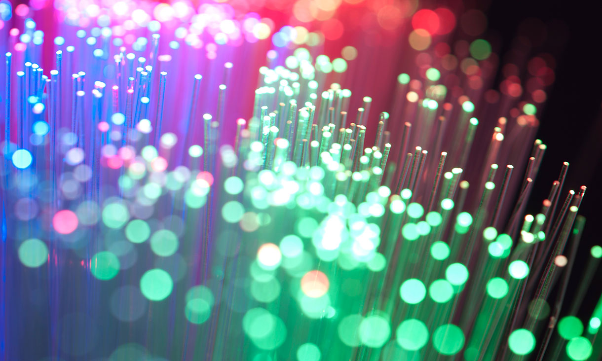 Close-up of glowing optical fibre cables with green, blue and pink light.