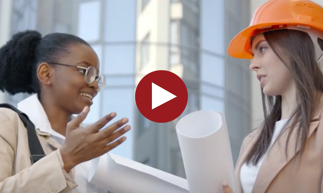 Two women in a discussion at a construction site, one wearing a hard hat and holding blueprints, with a red play button overlaid in the centre.