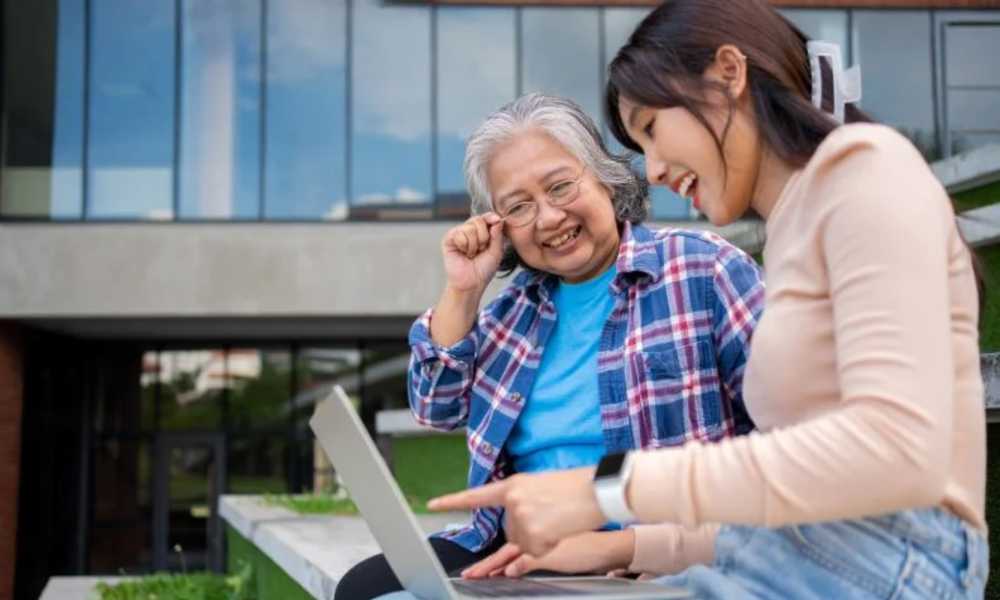 Young person helping elderly person with something on laptop