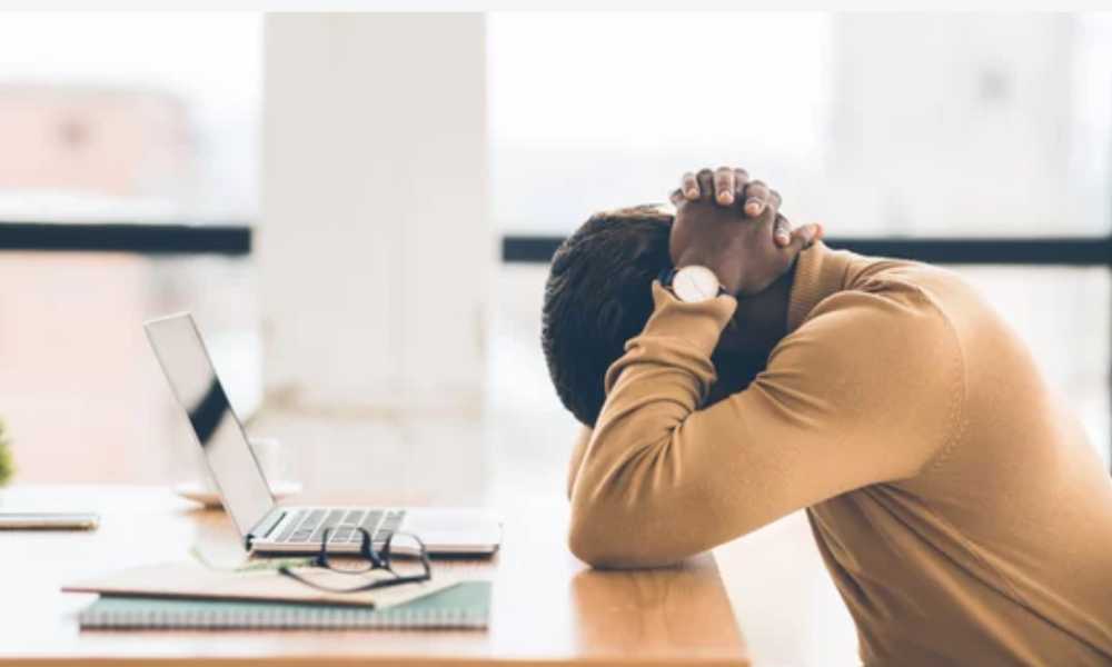 Person at their coputer desk with their head in their hands