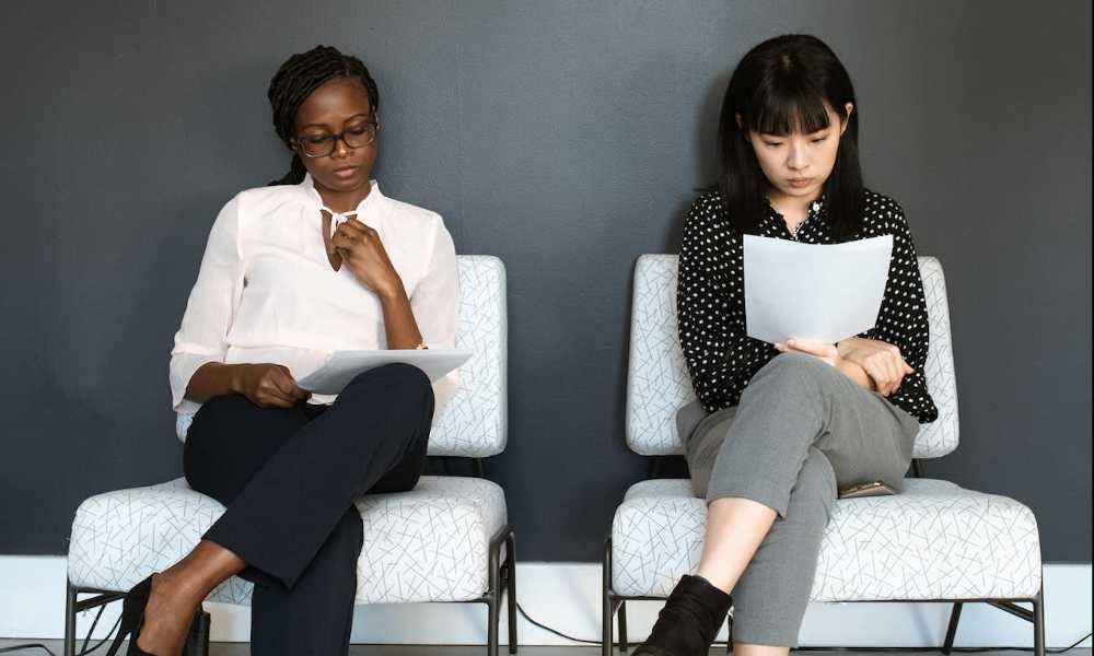 Two people sitting on chairs reading their CVs