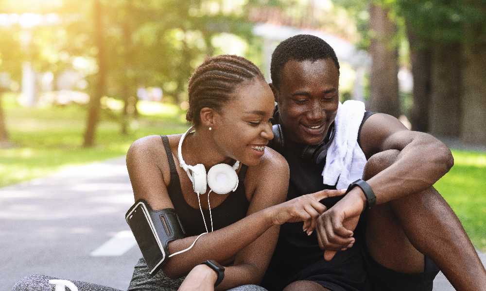 Two peole sitting on road wearing activewear, fitness watch and heart rate monitor
