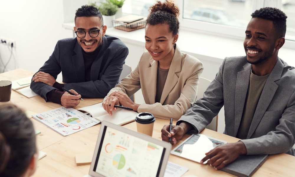 Three business people smiling at table with dashboards and ipads