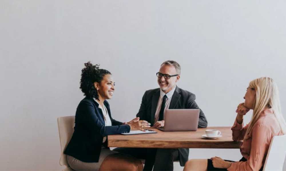 Three business people smilng around a table with a laptop