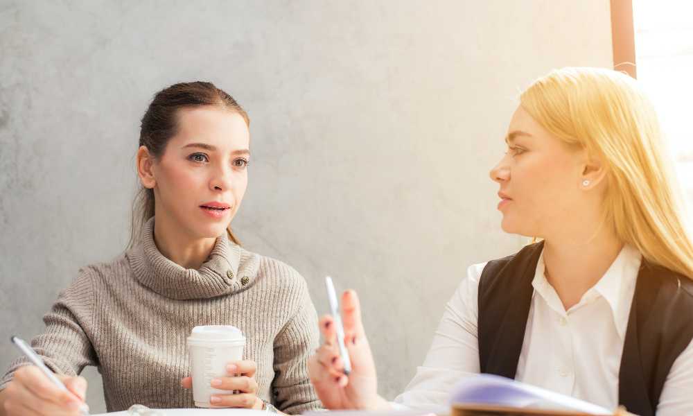 Two people talking to each other whilst holding pens and coffee cup