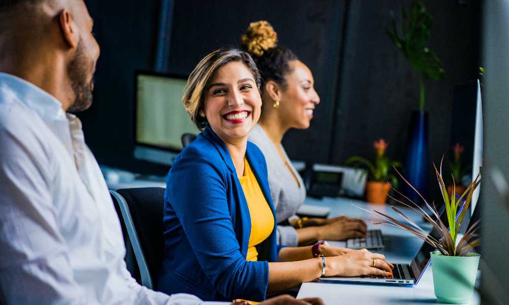 Person smiling working on laptop surrounded by other colleagues