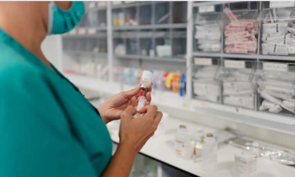Person wearing scrubs and mask holding vaccine vile