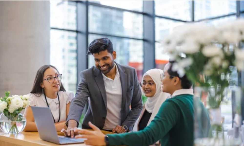 Group of four people gathered around a laptop
