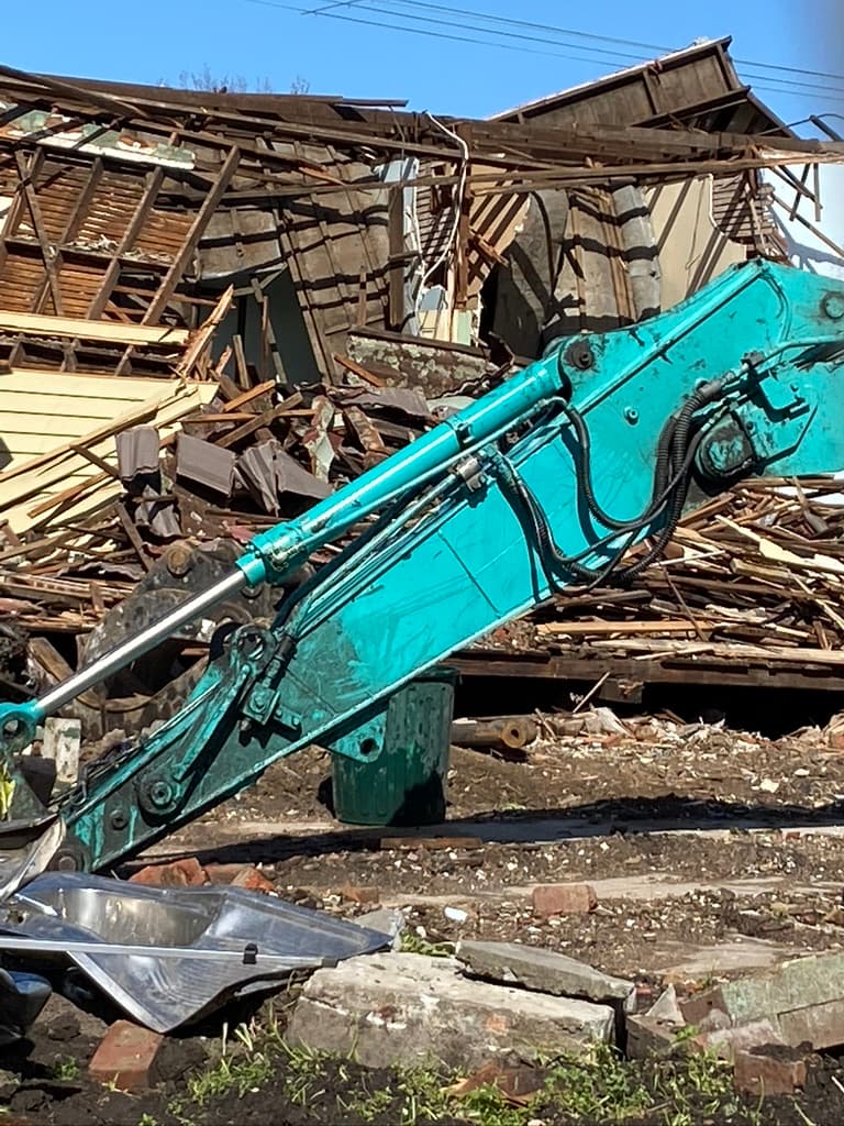 A backhoe in the middle of a demolished house