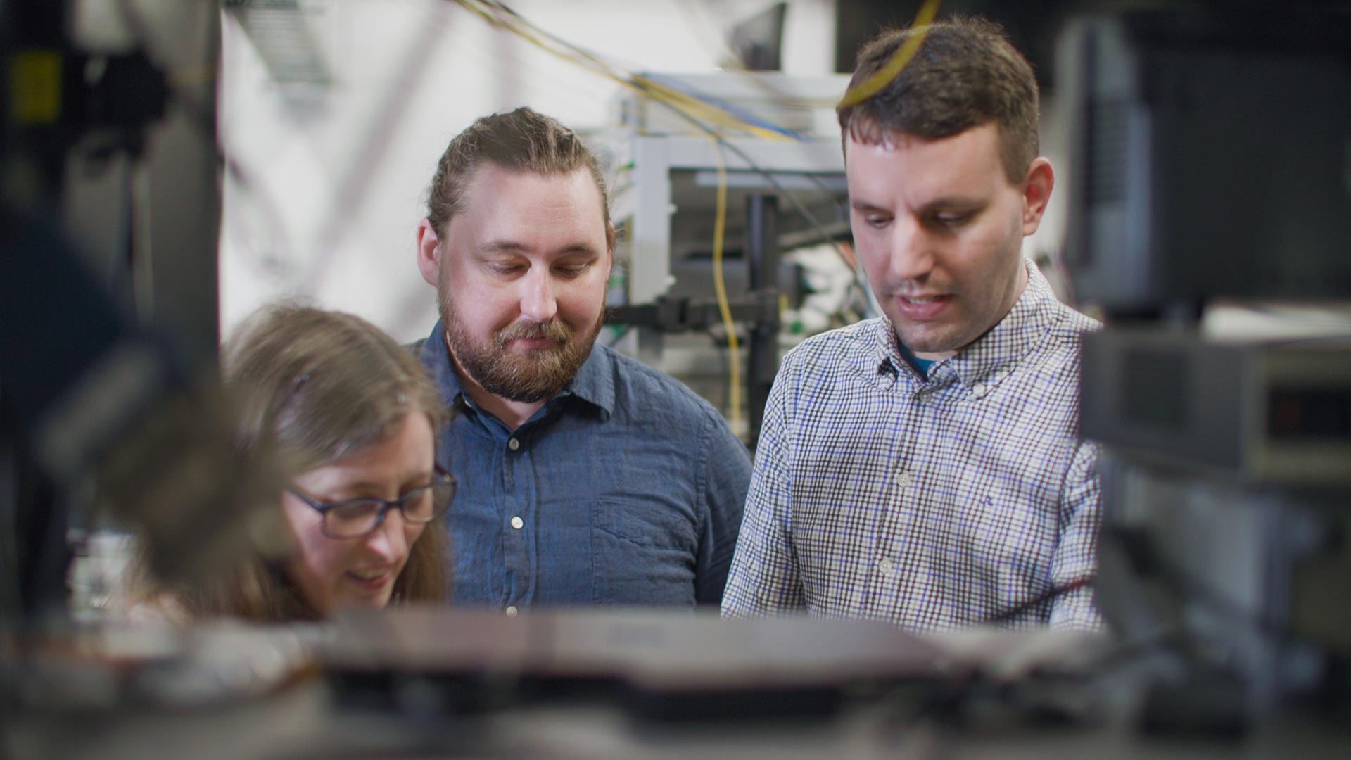 Three people standing together with computer equipment behind them