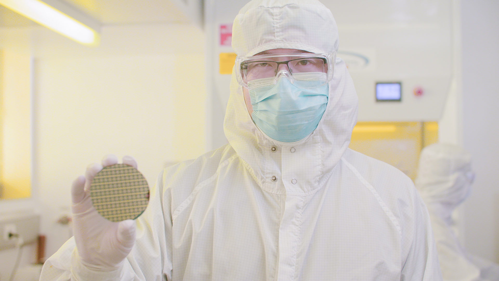 A person in white protective clothing holds up a circular object