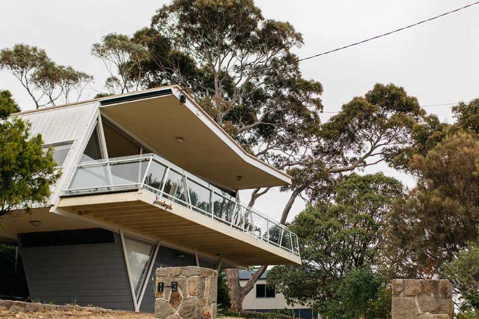 Picture of McCraith house. It is a pale, weatherboard house with a large balcony and surrounded by eucalyptus trees.