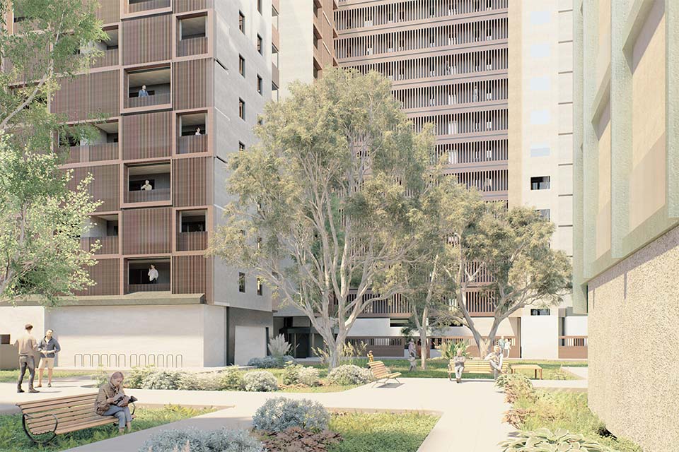 People walking and sitting in a landscaped courtyard surrounded by modern apartment buildings, with large trees providing shade and seating areas along the paths.