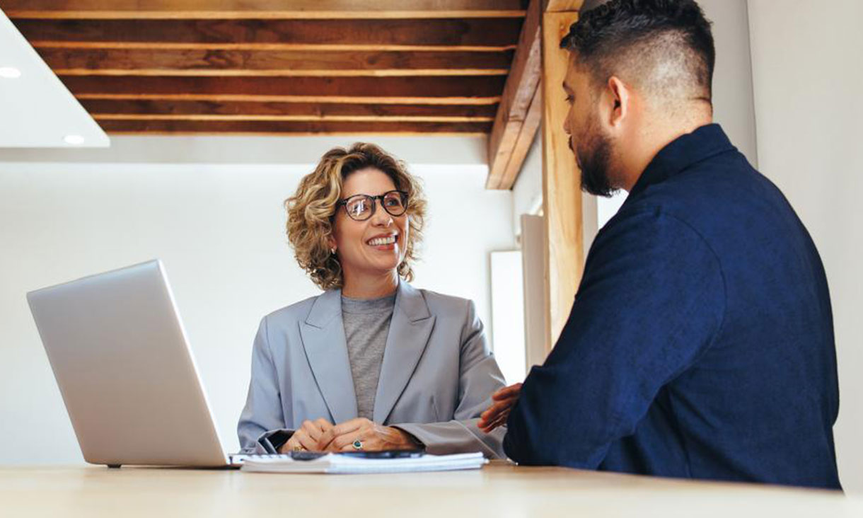 Corporate woman in blue blazer with laptop conferring with male co-worker.