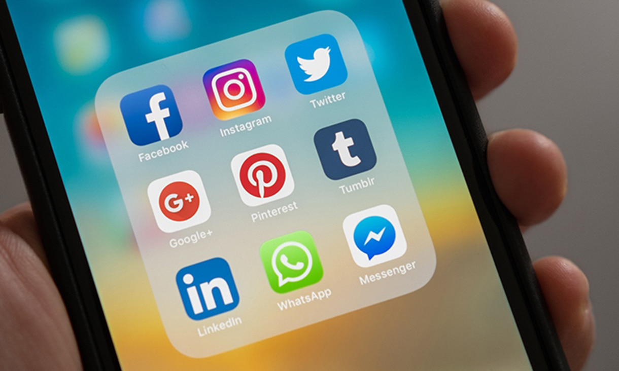  Close up of hand holding a smart phone showing social media app tiles.