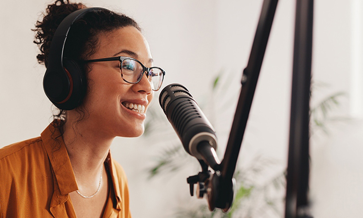 Woman in orange shirt wearing headphones and speaking into a microphone.