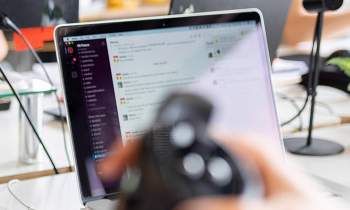 Blurry view of hand in foreground using joystick with a laptop in the background.