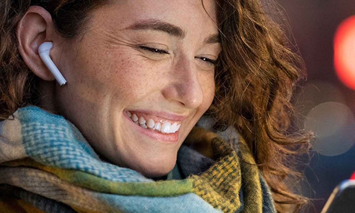 A woman smiling at her phone with her earphones in. 