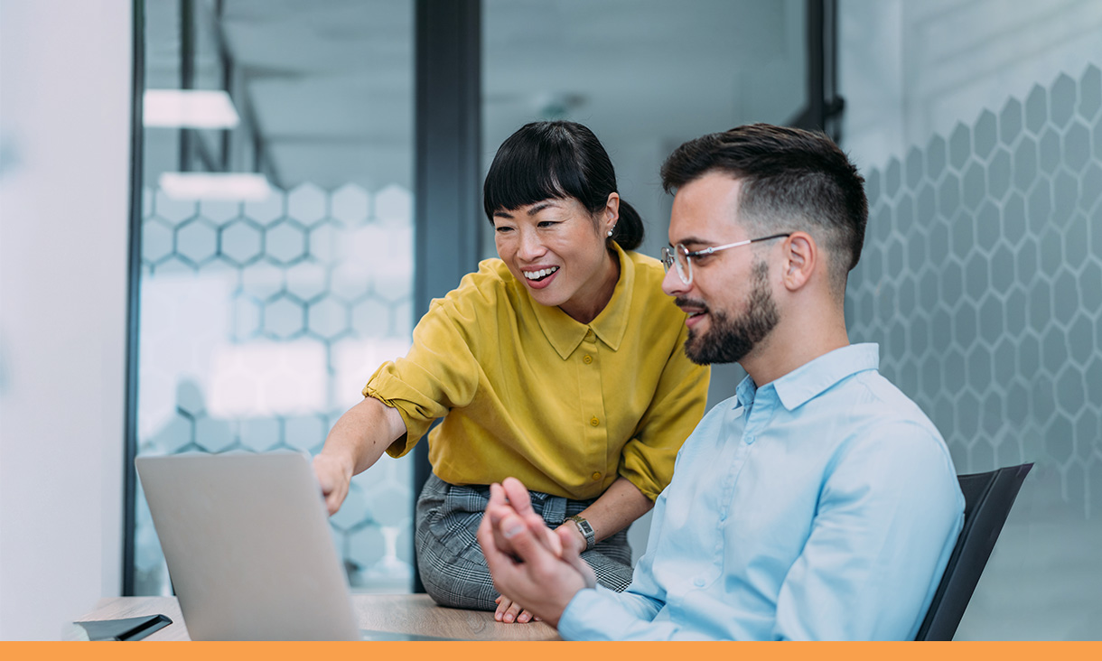 A woman points to a computer screen in discussion with her coworker.