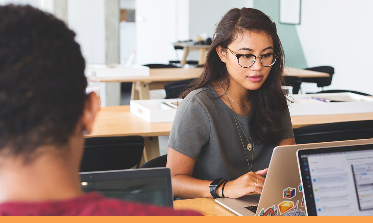 Two coworkers work opposite each other on their laptops in an office.