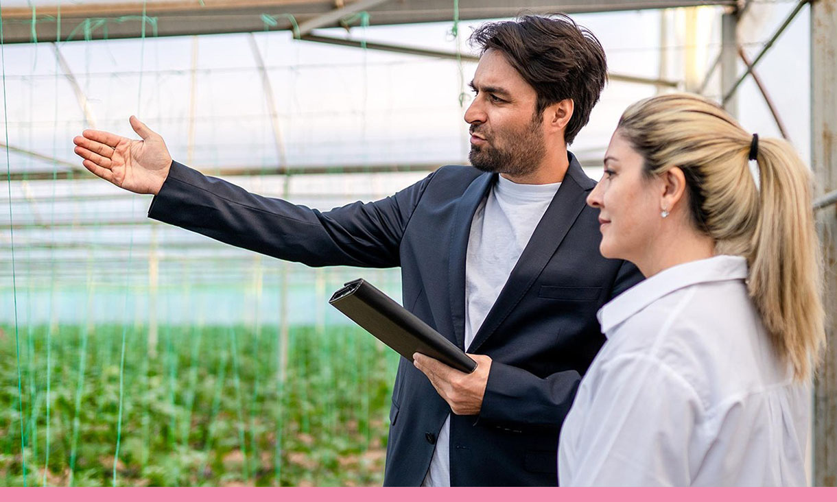 A man points to something off camera while talking to a coworker in a greenhouse.