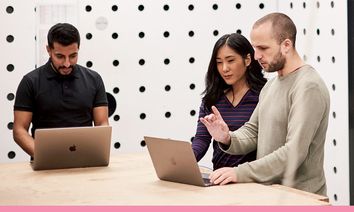 Three people in a meeting, two are looking at the same laptop.