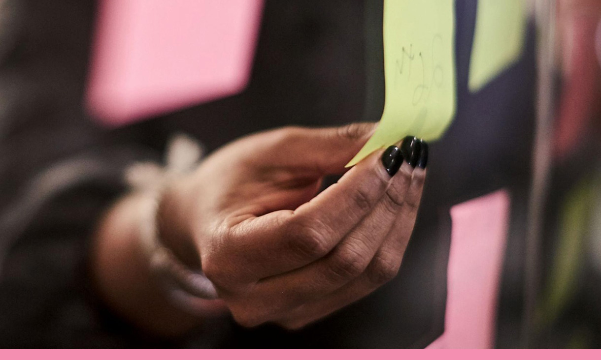 A hand adds a sticky note to a wall of sticky notes.