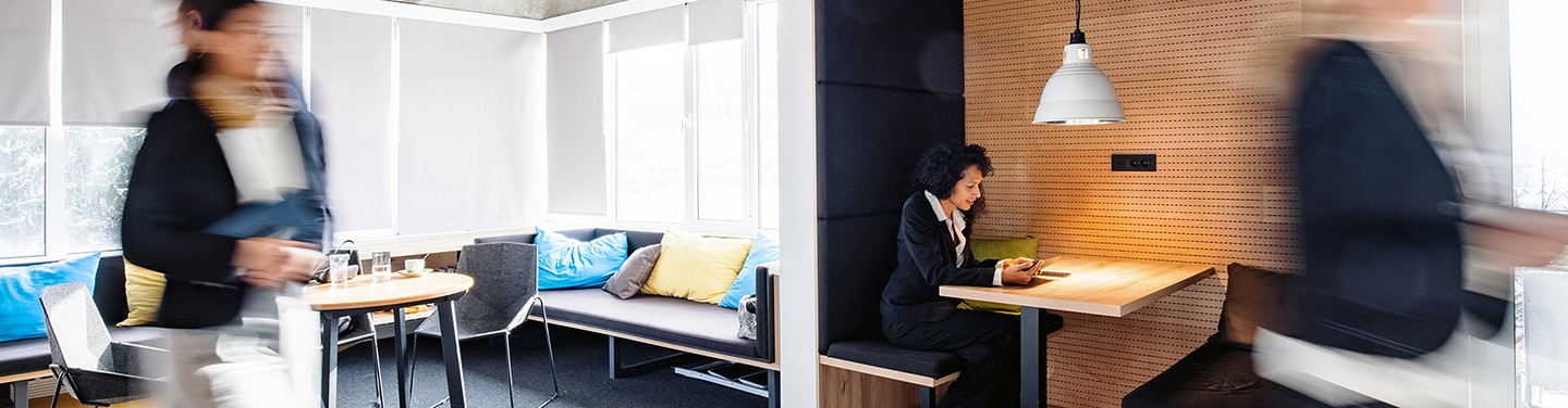 Two people walk past a lady working in a nook in an office.