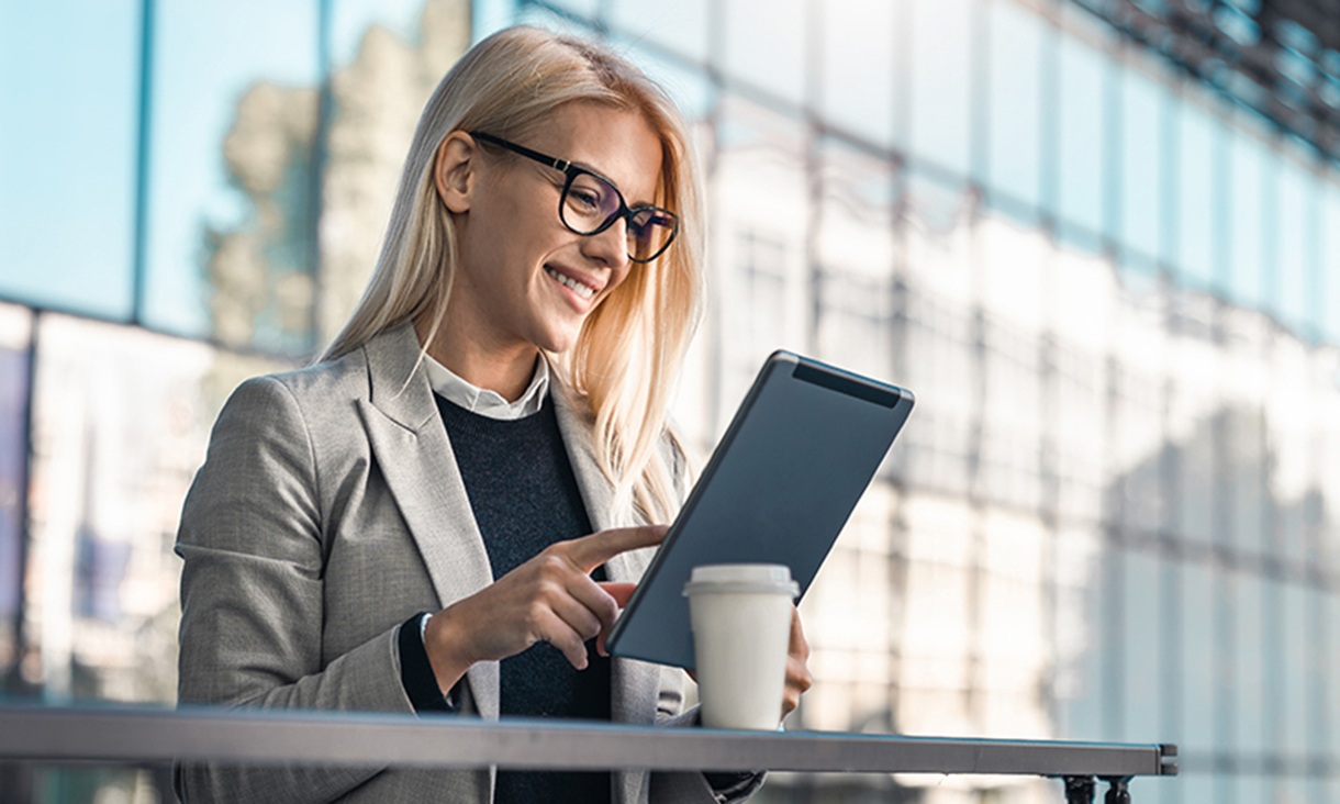 A woman stands on an office balcony and uses her tablet.