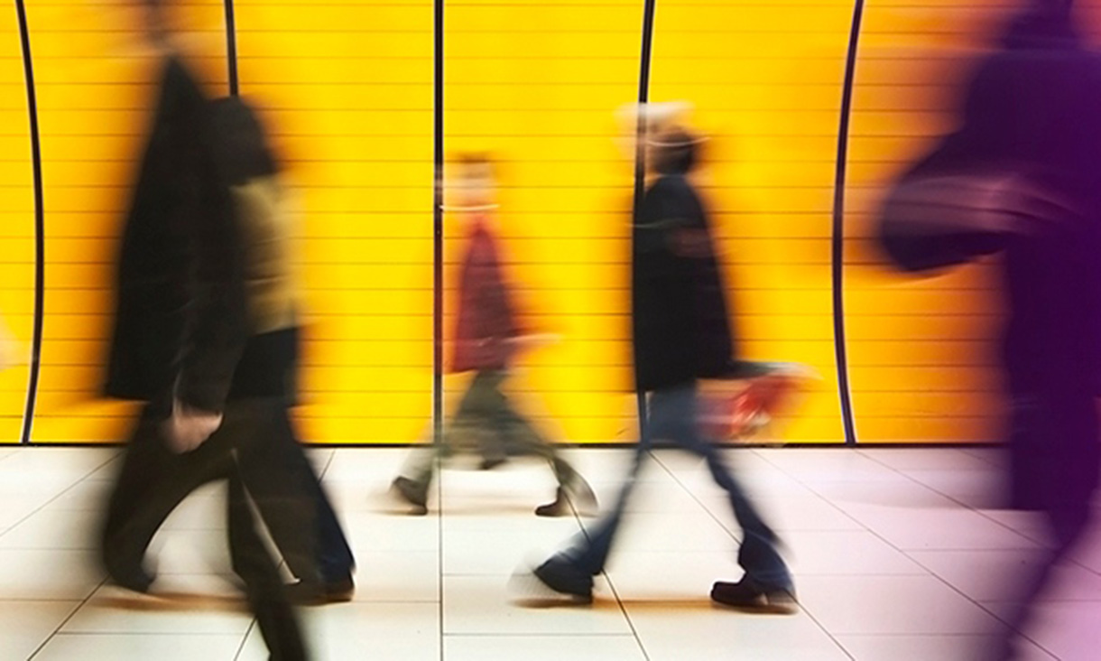 Long exposure image of gigures of people walking past yellow wall
