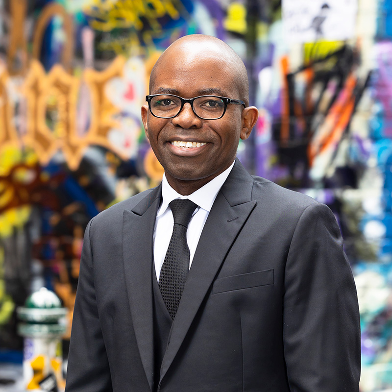 Portrait of Mathews Nkhoma standing in a city laneway in front of graffiti artwork