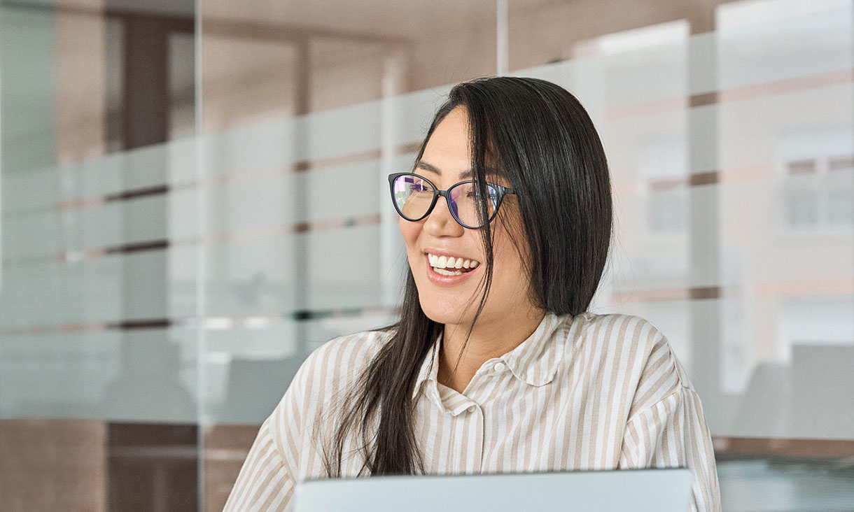 A student smiles while looking away from the camera, using a laptop.