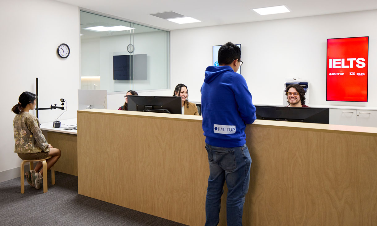 Students interact with IELTS staff at a desk, one posing for an ID photo.