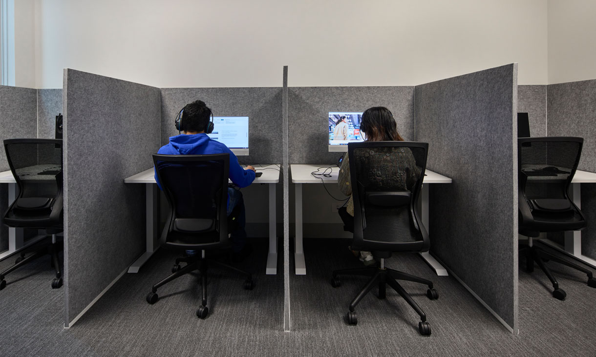 Two students, focused, sitting inside individual PTE exam booths with headphones on.